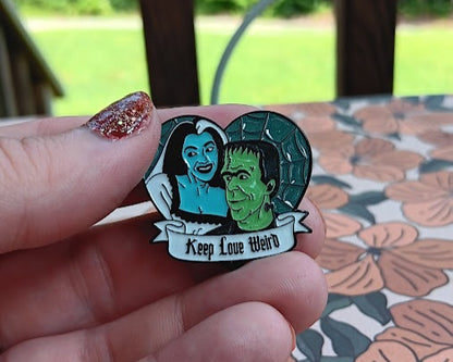 Pin with a design of a man and woman holding hands, with text 'Keep Love Weird', held by a hand against a floral-patterned surface.
