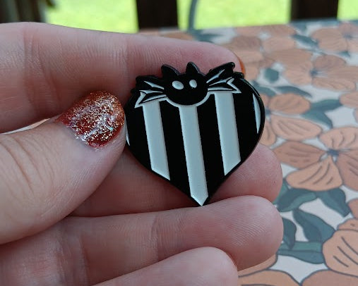 Black and white striped shield with a black cat design held by a hand on a floral-patterned surface.